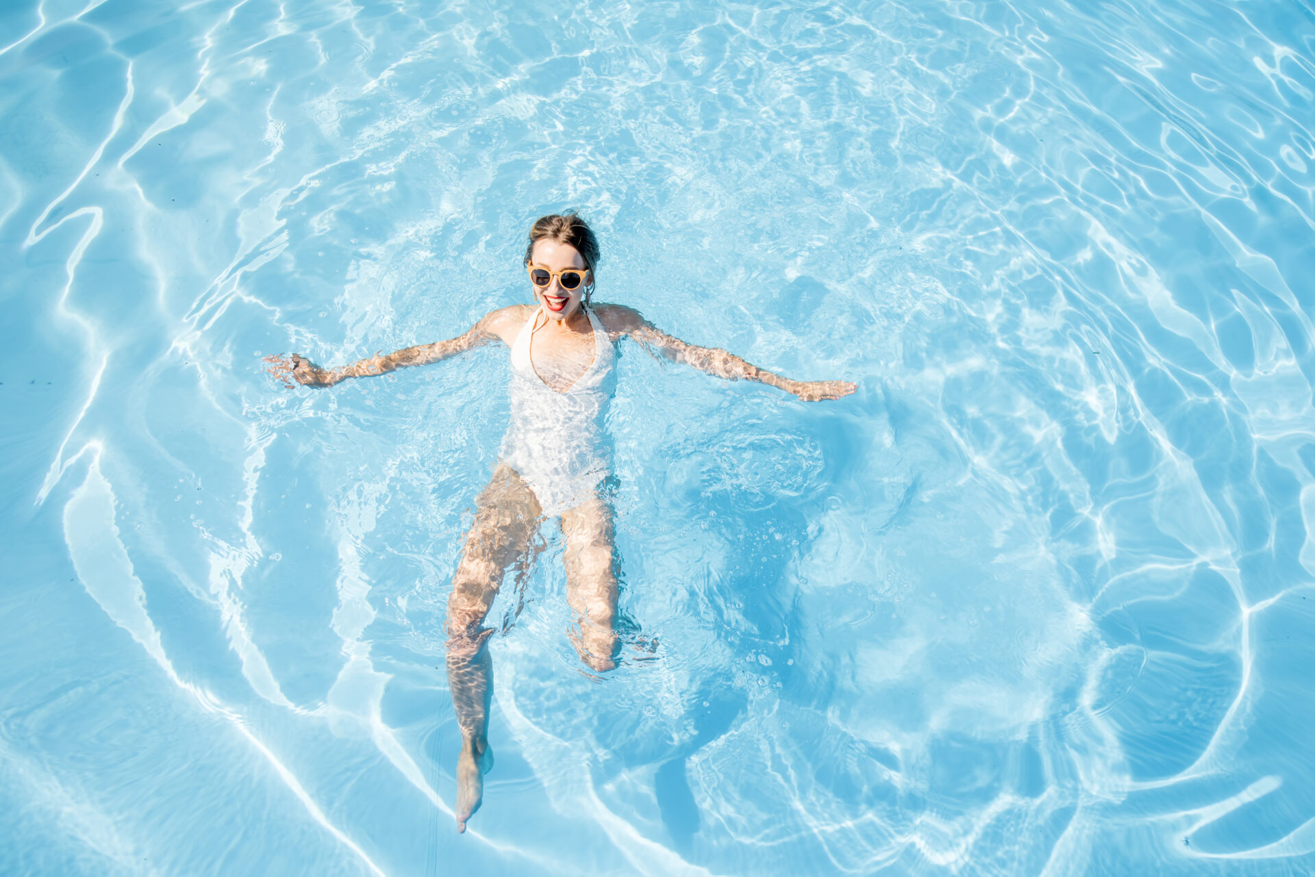 Young woman in swimsuit swimming at the basin with blue water. General view from above