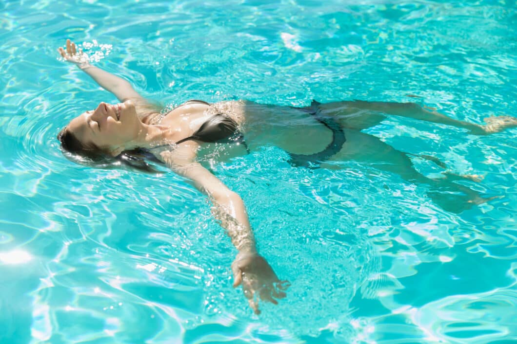 Carefree young woman floating on her back in a sunny swimming pool