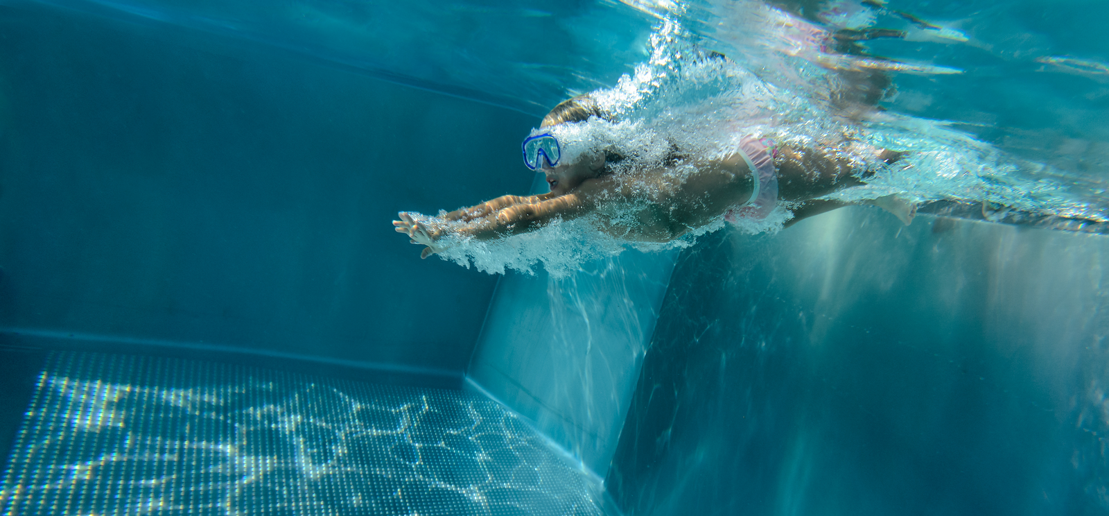 Young child in a diving mask and pink swimming costume diving into a swimming pool